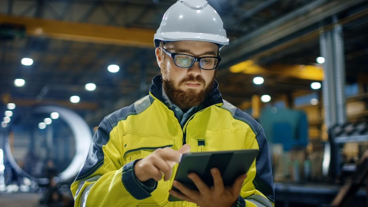 man dressed in safety vest and hard had reviewing data on a tablet