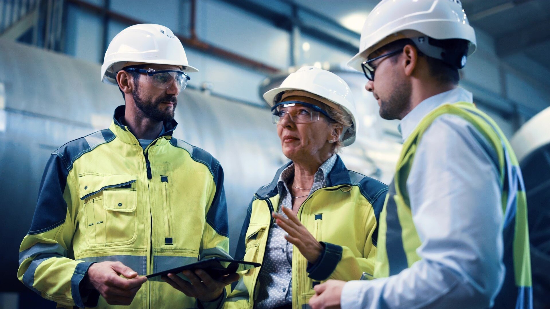 Three construction workers wearing high vis vests discuss invoicing on site