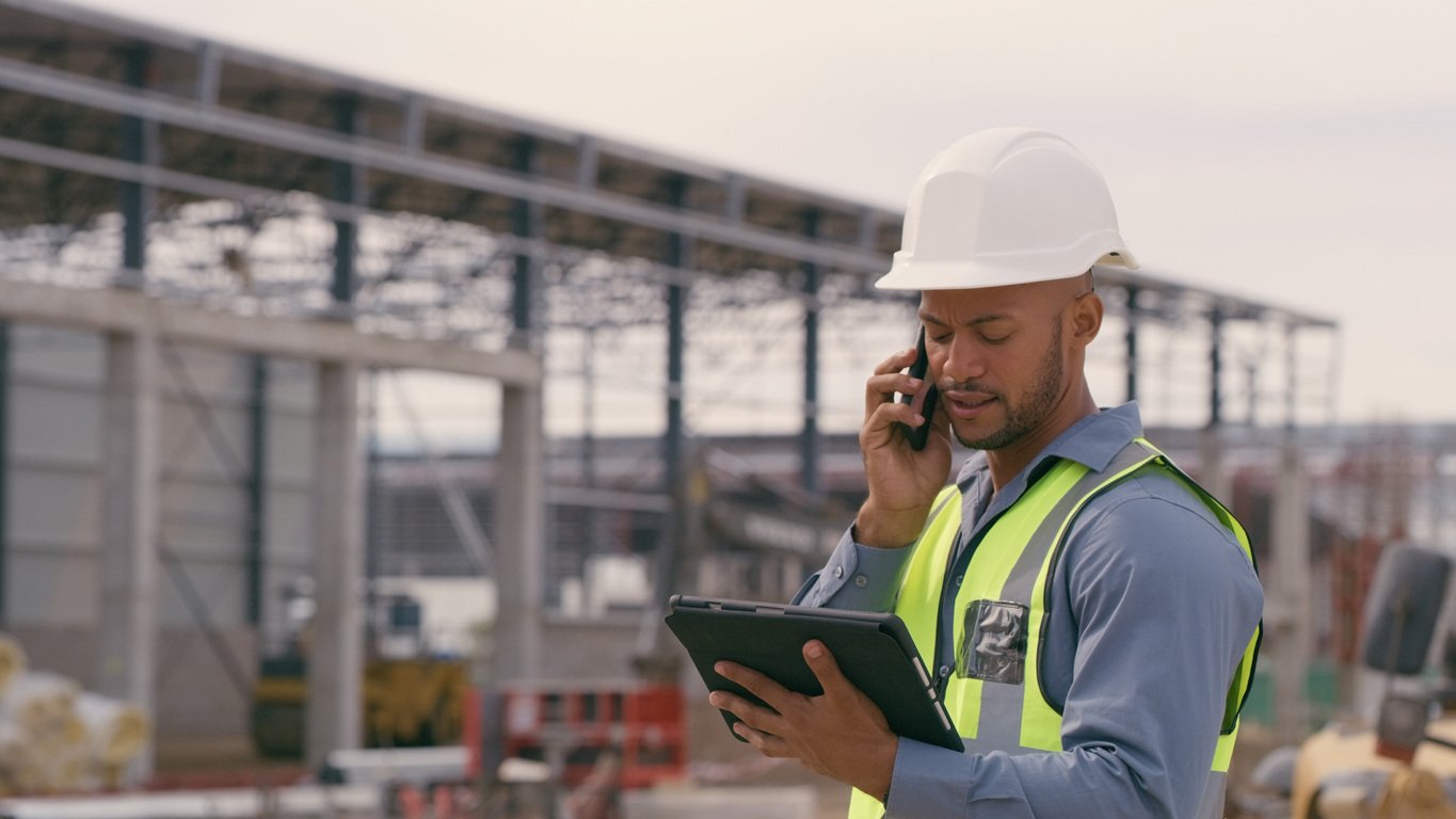 Construction manager on-site, using a tablet while on a phone call, monitoring project expenses and performance through Causeway Project Accounting
