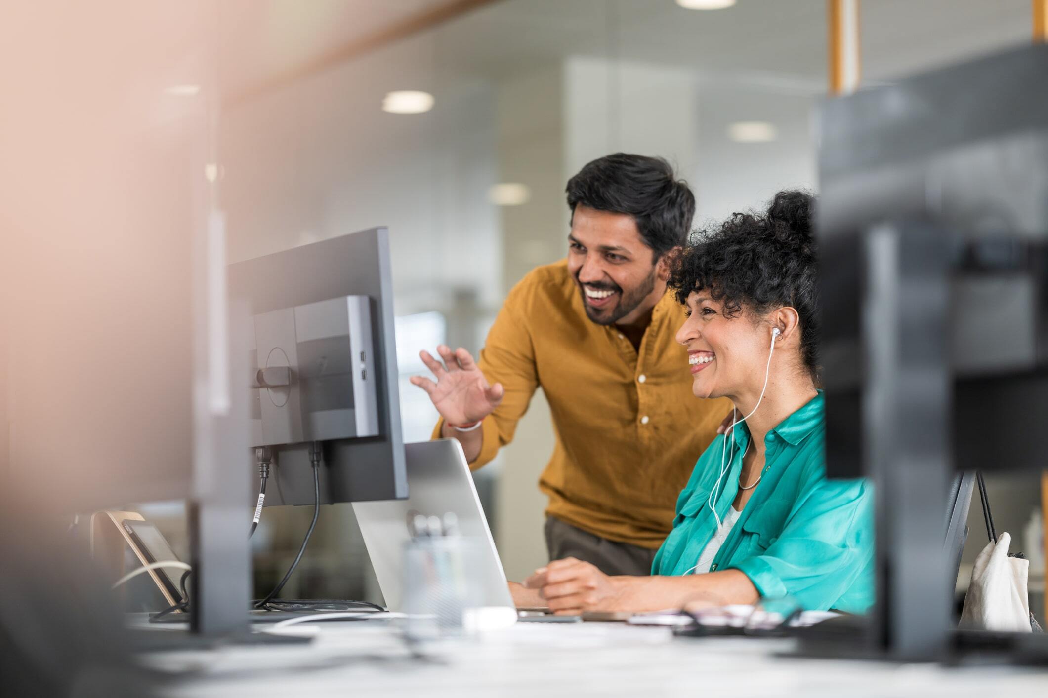Coworkers in front of computer monitor in modern office chatting online.-min