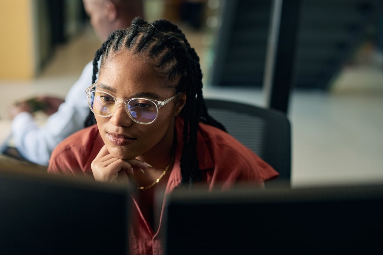 Lady wearing glasses sitting at a laptop in an office setting-min