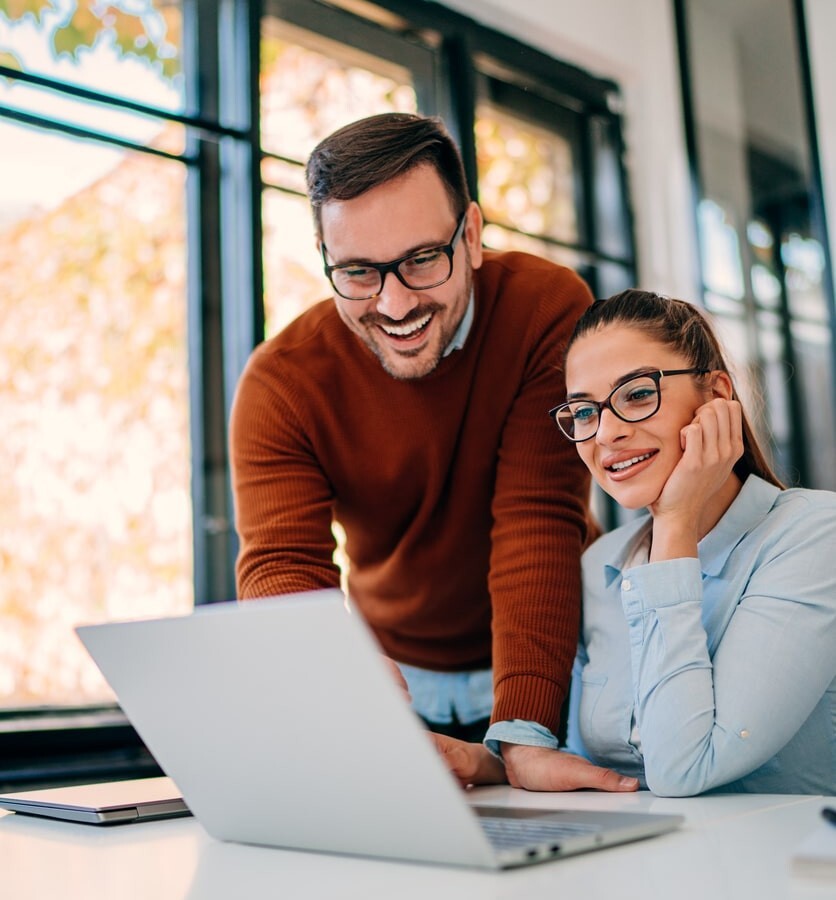 Male and female office workers smiling whilst looking at a laptop screen-min-1