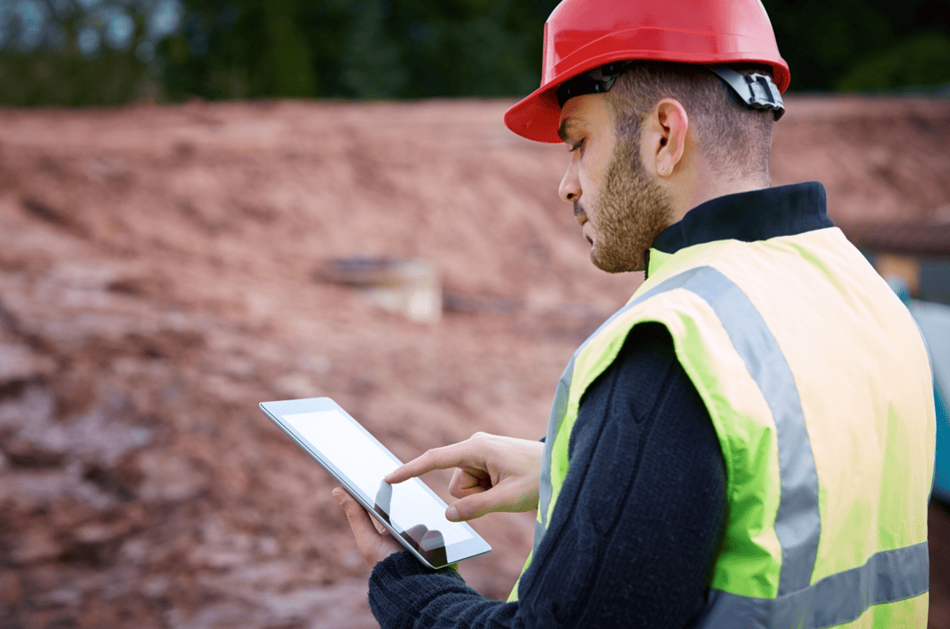 Male construction worker onsite in high vis holding a tablet