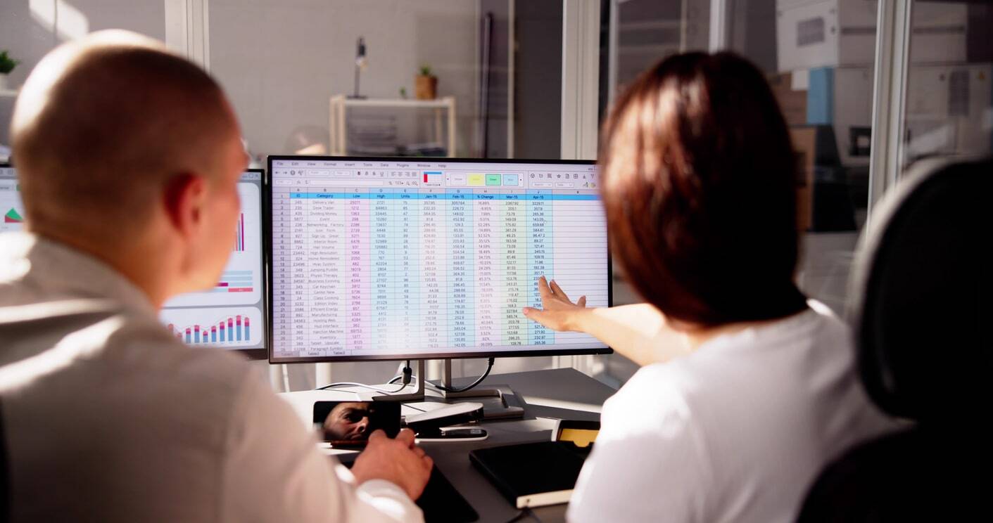 Image shows two people analysing a spreadsheet on a computer screen