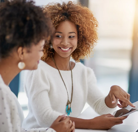 Two female workers chatting over a laptop and tablet in an office environment-3